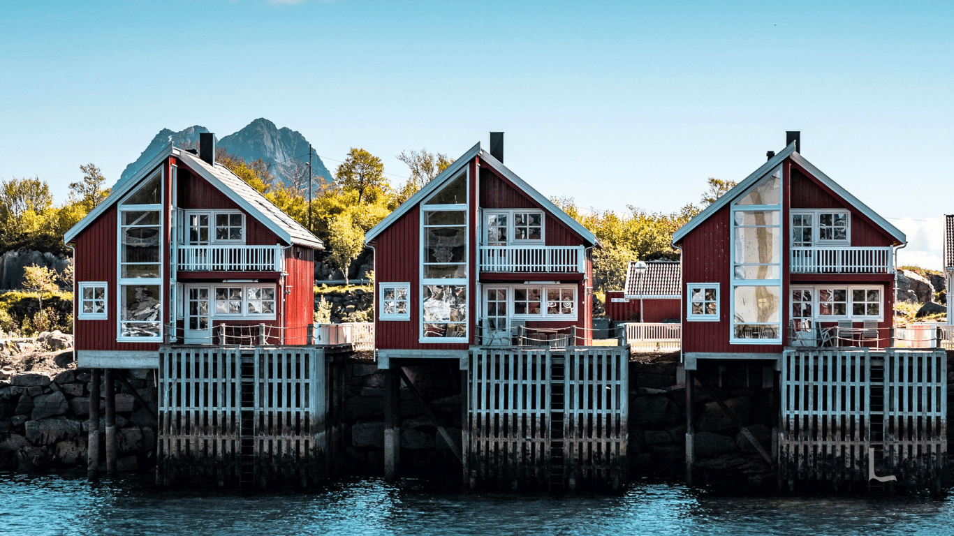 Tre røde trehus i vannkanten med egen brygge
